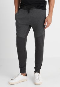 Slim-fit joggers i mörkgrått tyg med kontrasterande paneler och fickor. Har ett elastiskt midjeband med dragsko och ribbade muddar.