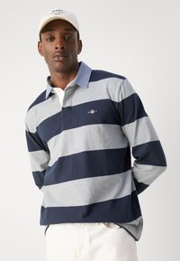 Tengerészkék és szürke csíkos hosszú ujjú galléros póló ellentétes színű gallérral, finom logóval a mellrészen és puha pamut textúrával.