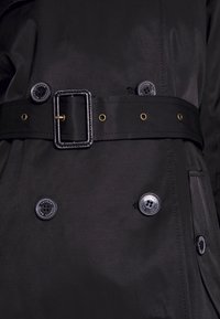 Svart trenchcoat med bälte, utrustad med knappar och detaljer i guld. Slät tyg med en elegant design och strukturerad form.