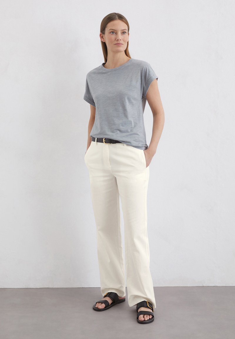 Graues Kurzarm-T-Shirt, cremefarbene weite Hose und schwarze Sandalen. Das Outfit zeichnet sich durch einen lässigen Schnitt und ein einfaches Design aus.