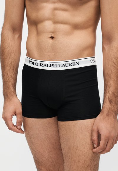 Мъжки торс, носещ черни боксерки Polo Ralph Lauren с бял колан, на който е изписано името на марката.