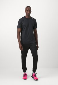 Camisa atlética negra de manga corta con textura de malla, combinada con pantalones negros y zapatillas deportivas rosa brillante, mostrando un estilo informal.