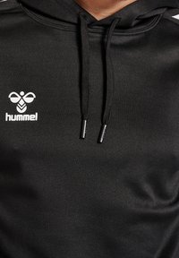 Sudadera negra de material suave con un logo en blanco en la parte frontal. Cuenta con una capucha ajustable y rayas blancas contrastantes en los hombros.