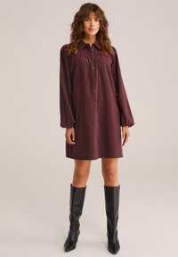 Abito rosso bordeaux con bottoni, a maniche a sbuffo, realizzato in tessuto testurizzato. Abbinato a stivali neri in pelle con tacco al ginocchio.