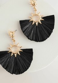 Schwarze fächerförmige Ohrringe aus strukturiertem Material, mit goldenen Strahlenakzenten und einem runden Zentrum. Leicht und detailliertes Design.