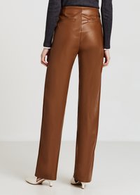 Braune, beigefarbene Lederimitat-Hose mit weitem Bein und hoher Taille, ausgestattet mit Gesäßtaschen und glatter Textur, kombiniert mit elfenbeinfarbenen spitzen Absätzen.