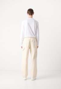 Pantalons cargo en coton beige avec poches latérales, design à jambe droite et étiquette de patch à l'arrière, associés à une chemise blanche à manches longues.