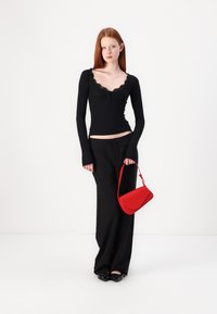 Black long-sleeve top with lace trim, black wide-leg pants, and a red handbag. Textured black shoes with studs complete the look.