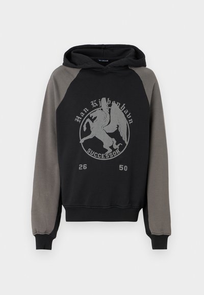 Hettegenser med svart kropp og grå raglanermer. Har et sentrert grafisk trykk av en vinget skapning, tekst og tall.