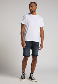 Camiseta blanca de manga corta combinada con pantalones cortos de mezclilla azul oscuro, enrollados en los puños, que se llevan con zapatillas altas negras. Diseño simple y casual.