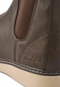 Bota de cuero marrón con paneles laterales elásticos, costuras de contraste y una suela de goma blanca con un logo grabado. Textura mate en general.