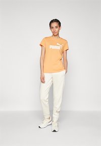 Oranžové bavlnené tričko s bielym logom "PUMA", skombinované s bielymi nohavicami s jemným detailom loga a bielymi teniskami.
