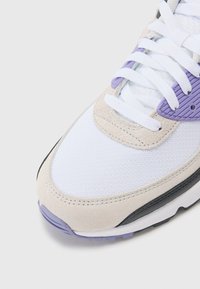 White sneaker with purple and beige accents, featuring a textured suede panel, mesh fabric, and white laces. Black sole visible.