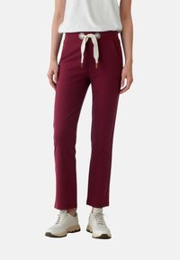 Vínové zúžené nohavice s bielym šnúrkami, dvoma bočnými vreckami a hladkou textúrou, v kombinácii so svetlými teniskami.