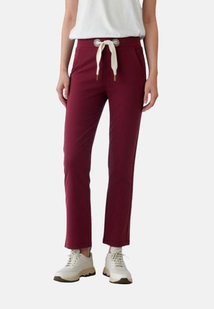 Weinrote, verjüngte Hose mit weißem Kordelzug, zwei Seitentaschen und glatter Textur, kombiniert mit hellfarbenen Sneakers.