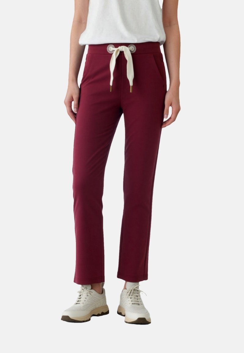 Vínové zúžené nohavice s bielym šnúrkami, dvoma bočnými vreckami a hladkou textúrou, v kombinácii so svetlými teniskami.