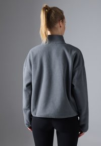Pullover in felpa grigia con colletto alto, spalle scese e vestibilità rilassata. Texture morbida e design semplice senza hardware visibile.