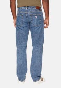 Jeans in denim blu con vestibilità a gamba dritta, dotati di due tasche posteriori, una patch in pelle sulla vita e un distintivo logo a triangolo.