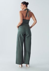 Zelený lněný overal se zavazováním na krku, širokými nohavicemi a zadními kapsami. Má přiléhavý korzet a lehkou texturu.
