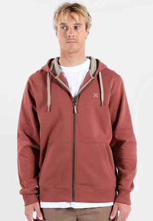 Sweat à capuche zippé couleur rouille avec des accents beiges ; doté d'une poche kangourou, d'une capuche à cordon de serrage et d'un logo brodé sur la poitrine.