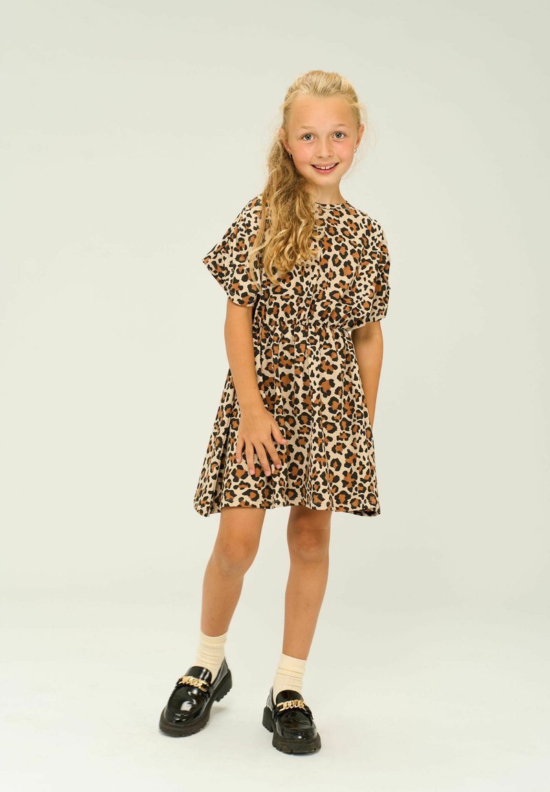 Läcker klänning med leopardmönster och korta ärmar, åtsittande midja och utsvängd kjol. Svarta loafers med guldaccenter och beige strumpor fulländar looken.
