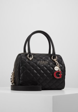 Czarna pikowana torebka Guess z podwójnymi uchwytami, odpinanym paskiem, srebrnym logo i czerwonym breloczkiem w kształcie litery "G" na białej powierzchni.