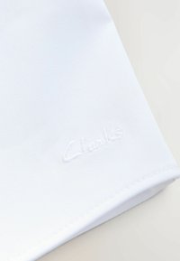 Vitt tyg med en texturerad yta, med en broderad logotyp "Clarks" i en något upphöjd design och snyggt sydda kanter.
