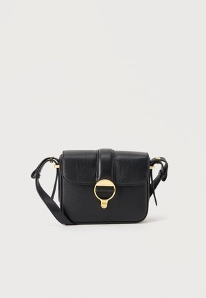 Czarna skórzana torebka na ramię z regulowanym paskiem i złotym okrągłym zapięciem na przedniej klapie, na jednolitym jasnym tle.