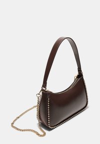 Borsa a mano in pelle marrone con tracolla in catena dorata, design curvo, chiusura con zip superiore e dettagli in metallo lungo i bordi.