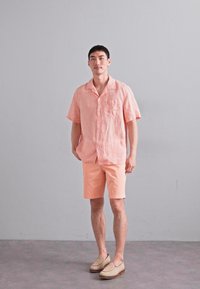 Lichtgewicht linnen overhemd met korte mouwen in pastelroze, gecombineerd met bijpassende shorts. Heeft een knoopsluiting aan de voorkant en een enkele borstzak.