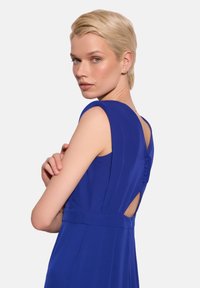 Sukienka w królewskim niebieskim kolorze, dopasowana, z okrągłym dekoltem, wycięciem na plecach oraz ozdobnymi guzikami wzdłuż kręgosłupa, wykonana z gładkiego materiału.
