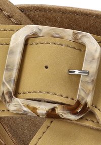 Correa de ante color marrón claro con una hebilla de mármol transparente. Detalle de costura visible; la hebilla tiene un cierre de pasador metálico y forma rectangular.