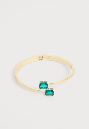 Bracelet jonc ouvert en or avec deux pierres précieuses rectangulaires bleu sarcelle aux extrémités sur un fond clair uni.