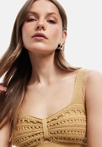 Top giallo in stile uncinetto con spalline larghe e un design a chiave centrale. La texture presenta motivi intricati e dettagli a costine.