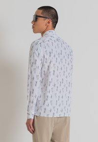 Camisa de manga larga de tejido blanco con patrón vertical negro. Presenta un cuello estándar y puños abotonados. Textura suave.