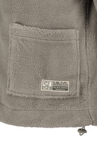 Graue Fleecejacke mit großer Fronttasche, Logoaufnäher und verstellbarem Kordelzug am Saum für eine individuelle Passform. Weicher, strukturierter Stoff.