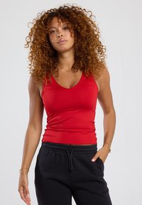 Red fitted tank top with a v-neck design, made from smooth, stretchy fabric. Paired with black drawstring sweatpants.
