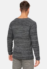 Pull-over long en gris avec des manches longues, présentant un motif rayé texturé, des poignets côtelés et un col rond. Le matériau semble doux et tricoté.