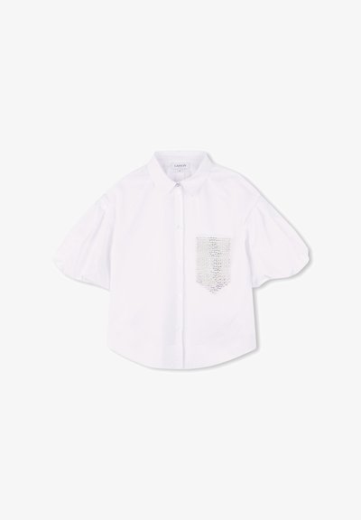 Blouse blanche à manches courtes avec un col, dotée d'une poche à rabat texturée sur le côté gauche. Fabriquée en tissu lisse avec un léger éclat.