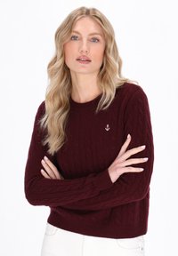 Burgunderfarbener, kabelgestrickter Pullover mit Rundhalsausschnitt und gerippten Bündchen. Eignet sich mit einem kleinen silbernen Ankeremblem auf der Brust.