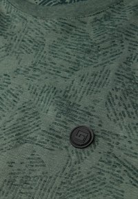 Zielony t-shirt w wzory wykonany z teksturowanej tkaniny. Posiada okrągły dekolt oraz czarną okrągłą naszywkę z logo na przodzie jako detal.