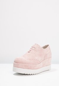 Chaussures à plateforme en suede rose clair avec un design brogue, dotées d'un bout arrondi, de perforations subtiles et d'une semelle blanche à zigzag.