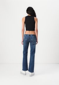 Top corto nero, jeans blu a zampa d'elefante con tasche, leggera usura e sneaker bianche con dettagli neri.
