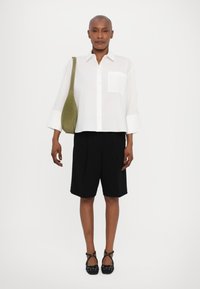 Hvit skjorte med brede ermer, svarte skræddersydde shorts og svarte sko med utsmykninger. Grønn skulderveske og minimalistisk lomme detaljer.