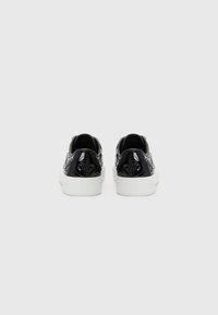 Svarta sneakers med en texturerad läderfinish, med vita gummisulor och blommönster på sidorna. Inga snören visas.