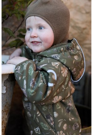 Jachetă impermeabilă verde măsliniu cu modele inspirate din natură. Are închidere cu fermoar, glugă și un captuseală moale. Pălărie tricotată maro completează aspectul.