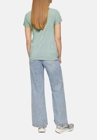 Chemise mint à manches courtes associée à un jean large bleu clair. La tenue présente une coupe décontractée et un minimalisme dans les détails.