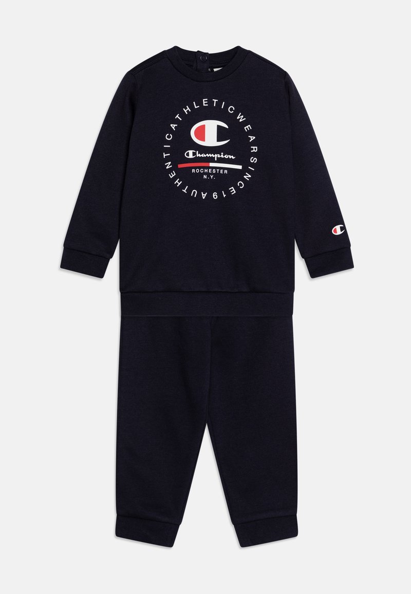 Tuta a due pezzi blu navy realizzata in tessuto morbido. Presenta maniche lunghe, polsini elasticizzati e un grande logo sulla parte anteriore.