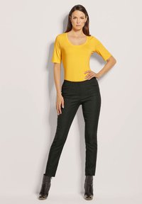 Gelbes kurzärmliges Oberteil mit einem Rundhalsausschnitt, kombiniert mit hochgeschnittenen schwarzen Skinny-Hosen und schwarzen Stiefeletten mit spitzem Zeh.
