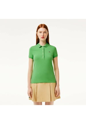 Polo verde in cotone, con colletto classico, patta con tre bottoni e un piccolo logo ricamato. Abbinato a una gonna plissettata beige.